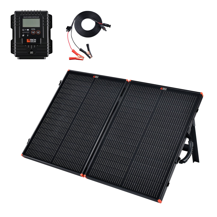 A black two-fold briefcase solar panel opened and propped on its integrated rear kickstand, with orange corner protectors. Above it sit a black weather-sealed charge controller with an LCD, and a coiled cable ending in red and black alligator clamps at one end and an MC4 connector at the other.